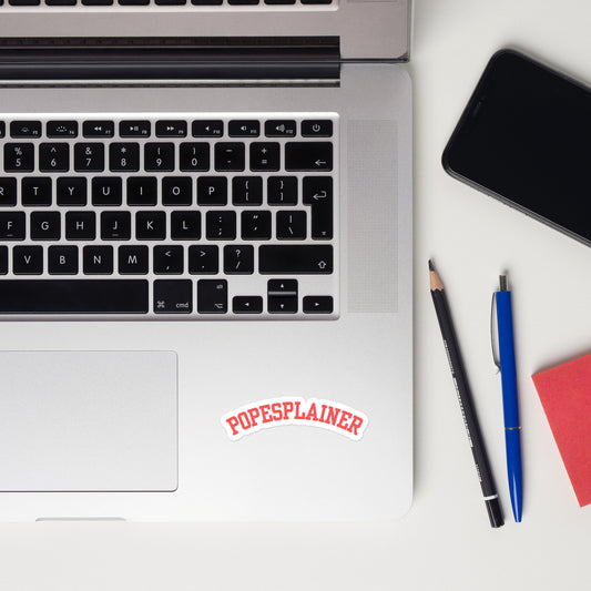 Laptop computer, on a desk, with a "popesplainer" sticker in a red serif font, on a white background.